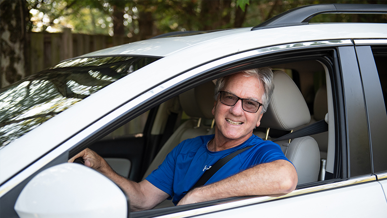 A middle-aged man is smiling as he drives a car. An easygoing guy, he's happy to provide rides to elderly in the Northern Virginia area so they can meet friends, go to the store and attend appointments. He's happy because transportation for seniors is now solved!