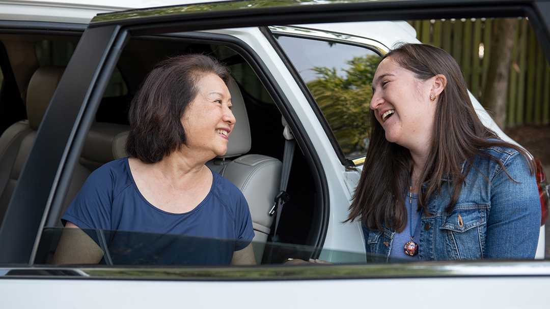 A young woman smiles at the passenger in the back seat as she exits the car. They've become friends through the NV Rides program that provides transportation services through its partner organizations. Both are happy because transportation for seniors is now solved!