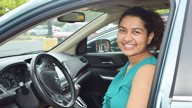 Smiling NV Rides volunteer, Rhea Sharma. She is sitting in the driver seat of a car. She's happy because transportation for seniors is now solved!